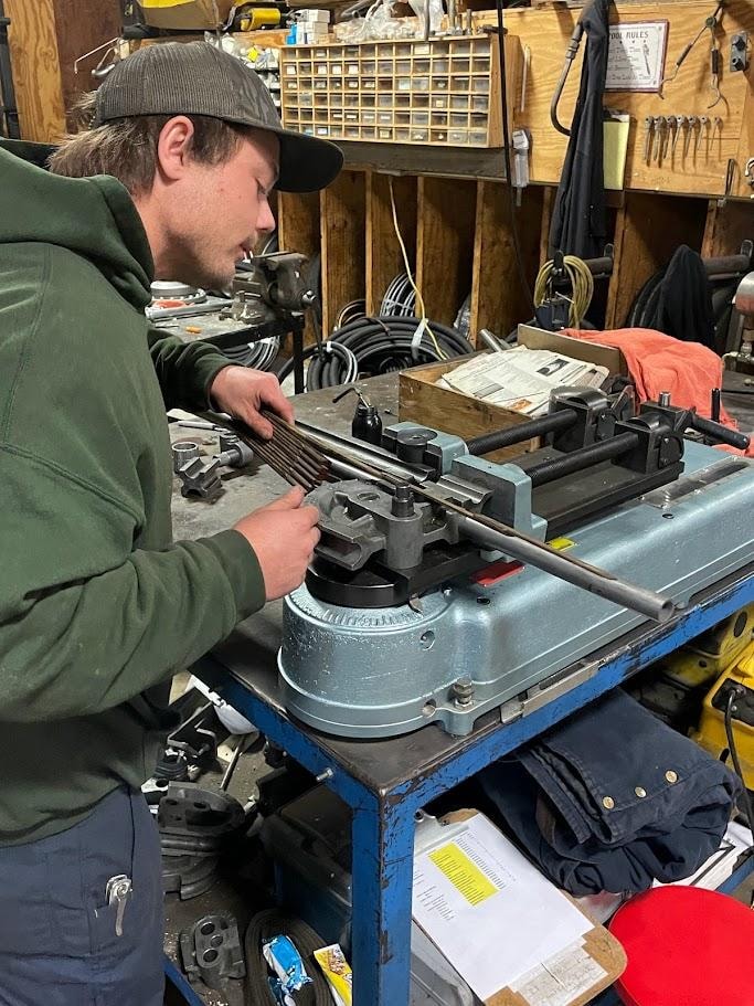 B&B Hose technician bending steel hydraulic tubing on a manual tube bender at the shop