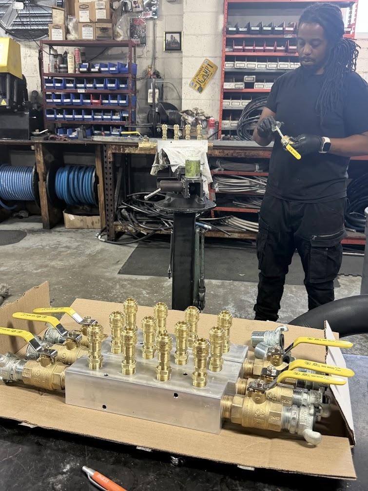 Technician assembling a custom brass air manifold block with ball valves in the B&B Hose shop